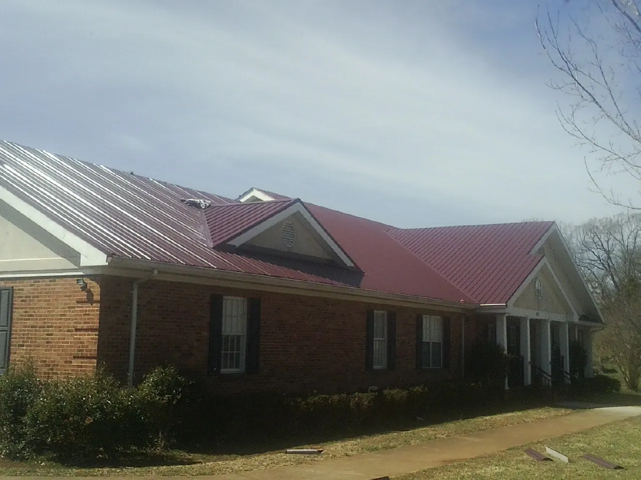 Red metal roof with gabled entries on a long brick building, from a Hail Damage Roof Repair job in Key Biscayne